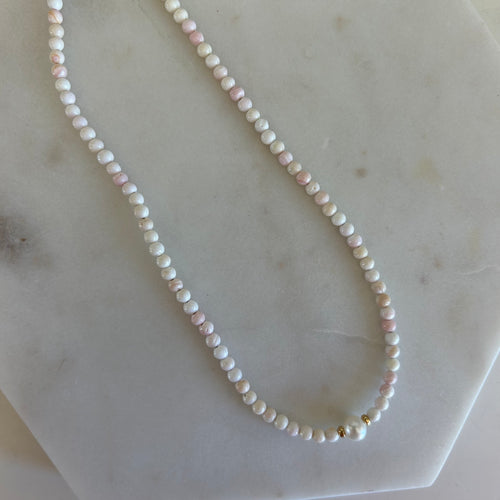 White beaded necklace with a pearl in the center. Flat laid on a marble white background. 