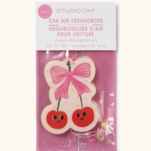 Load image into Gallery viewer, 
















































































































Studio Oh! car air fresheners in a clear baggie with a white paper top and the words: 'STUDIO OH!" , "CAR FRESHENERS", and " Fresh Picked Fruit" in pink print. The baggie's background is pink, and inside is an air freshener resembling a double cherry. Cherries are red with black smiling faces, green stems, and a pink bow, and a cream background.  Package against a white background.