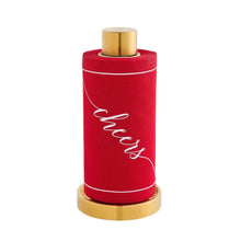 Load image into Gallery viewer, Roll of red cotton cocktail napkins with a white border and "cheers" in white script displayed on a gold stand against a white background. 