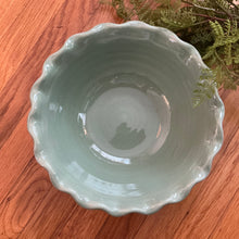Load image into Gallery viewer, Green stoneware bowl with a scalloped rim viewed from above on a wooden surface with greenery on the upper right side. 