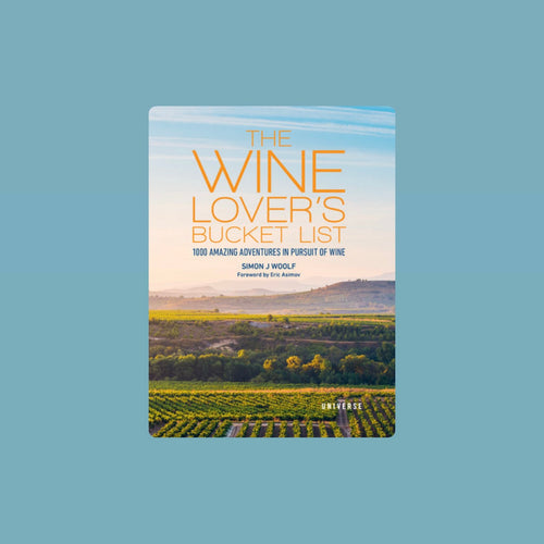 Book cover of The Wine Lover's Bucket List by Simon J. Woolf, featuring an expansive vineyard landscape with rows of green grapevines under a soft blue sky with wispy clouds with orange-colored lettering. Book displayed against a light blue background.  