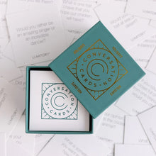 Load image into Gallery viewer, Dark Blue box with a gold foil print that reads &quot;Conversation Cards&quot;. The box is opened and inside is a stack of white cards with a similar blue print. The box is on a background of the cards spread out. 