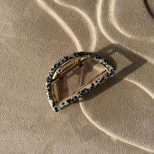 Load image into Gallery viewer, Leopard-print half-moon metal claw clip with gold hardware displayed on a beige textured surface with soft curved light reflections.