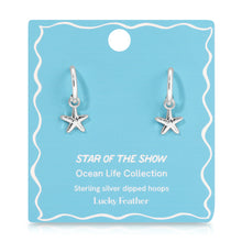 Load image into Gallery viewer, Pair of sterling silver-dipped hoop earrings with small starfish charms displayed on a light blue &quot;Star of the Show&quot; Ocean Life Collection card by Lucky Feather with white wavy border detailing, displayed against a white background. 