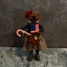 Load image into Gallery viewer, Preppy Bears Ornaments, lifestyle image of a brown teddy bear wearing a red beret, navy knit sweater with an American flag design, white collar, beige skirt, and dark boots, holding a red-and-white striped candy cane and a brown handbag with a cream button, displayed on a gray stone surface against a gray patterned background.
