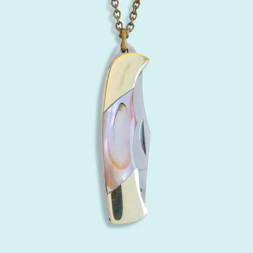 Small gold and abalone charm in the shape of a pocket knife. Light blue background. 