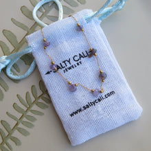 Load image into Gallery viewer, Gold chain necklace with purple stones and gold accents on a Sally Cali Jewelry pouch.