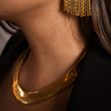 Load image into Gallery viewer, Model wearing a wide gold-plated brass herringbone chain necklace, shown close-up against a warm, softly lit background with matching gold fringe earrings. 