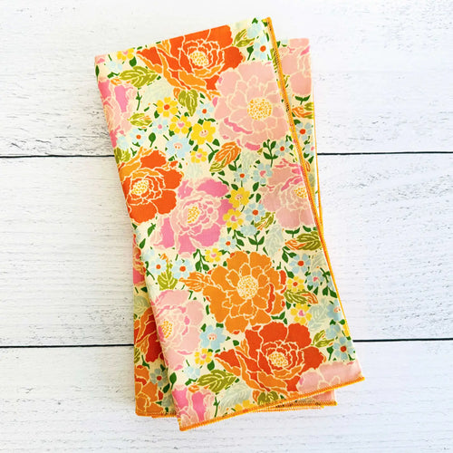 Pink and orange flower print folded cloth napkin on a  white wooden background. 