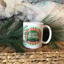 Load image into Gallery viewer, White coffee mug with a green print that reads &quot;Happy Holidays from Kensington.&quot; Background is an abstract painting and pine needles. 