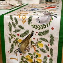 Load image into Gallery viewer, 12 Days of Christmas table runner featuring illustrated partridges, pears, and evergreen sprigs on a white background with a green border, displayed draped across a dining table.
