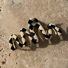 Load image into Gallery viewer, Checkered black-and-white wavy claw clip with gold metal hardware displayed on a beige travertine surface with soft shadows.