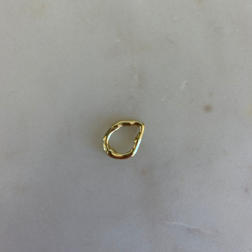Organically shaped gold ring on a white marble background. 