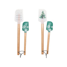 Load image into Gallery viewer, Two sets of silicone spatulas with a winter theme design. Each set has a regular sized white spatula and a mini green spatula . The set on the left has musical notes on the regular sized white spatula ,and snowflakes on the mini green spatula. The second set on the right side has a pine tree on the white full size spatula ,and snowflakes on the green mini spatula . Both sets have wooden handles with holes bored at the bottom with string tied in a loop for hanging. Both sets against a white background. 