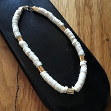 Load image into Gallery viewer, Necklace with white beads and gold accents on a black display , on a wooden background.