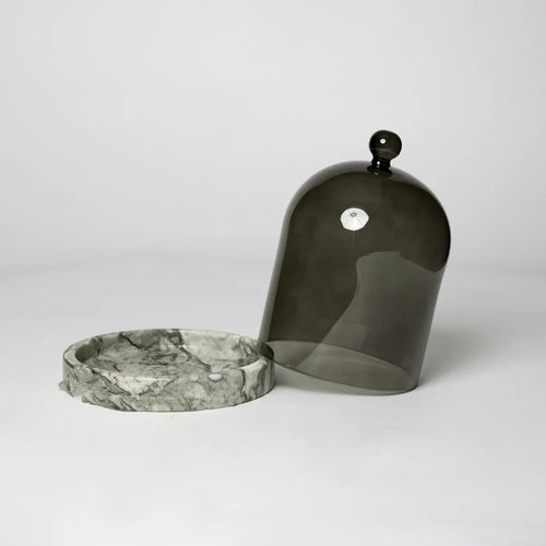 A black glass cloche with a black marble base, displayed on a white background.