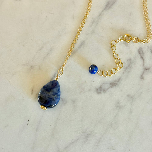 Gold necklace with a blue sodalite teardrop pendant on a marble surface