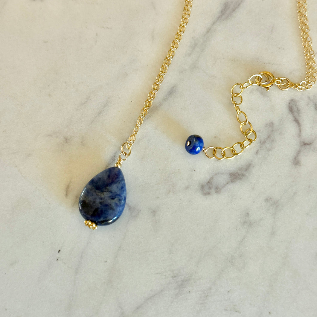 Gold necklace with a blue sodalite teardrop pendant on a marble surface