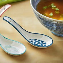 Load image into Gallery viewer, White stoneware Geo Soup spoons with teal and blue rims and geometric  patterned interiors beside a bowl of soup, displayed on a neutral background. 