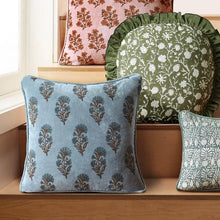 Load image into Gallery viewer, Velvet throw pillows with Mughal floral designs in muted blue, green, and blush tones arranged on a wooden surface against a light wall and window.