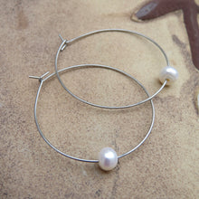 Load image into Gallery viewer, Silver hoop earrings with a single pearl on a textured beach surface