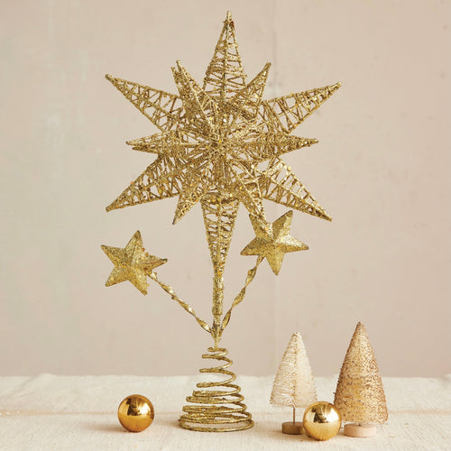 Gold Christmas tree topper with large star and two smaller stars , on a white surface and two gold miniature Christmas trees and two gold round ornaments against a white background.