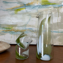 Load image into Gallery viewer, Splash Cup clear hand-blown glass with abstract pistachio green and white swirled design, stacked on one another beside a matching pitcher on wooden surface against abstract background. 