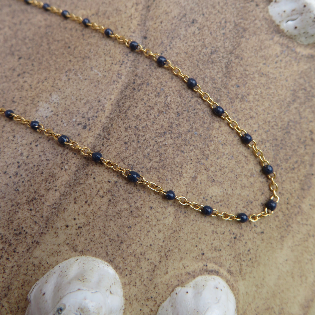 Gold chain necklace with dark blue beads on a beach surface