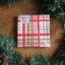 Load image into Gallery viewer, Square &quot;Merry Berry Bright&quot; cocktail paper napkin set with a red, pink, green, and white plaid pattern, displayed on a wooden surface with garland and a pinecone.  