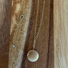 Load image into Gallery viewer, Gold chain necklace with a round mother of pearl pendant on a wooden surface.