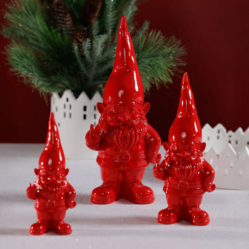 Three glossy red gnomes in various sizes with tall pointed hats, beards, and belts, each playfully holding up a middle finger, displayed on a white surface in front of greenery and white house silhouettes.  