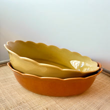 Load image into Gallery viewer, An olive-colored stoneware dish with scalloped edges stacked on a terracotta-colored dish of the same style, both resting on a brown textured surface against a white background. 