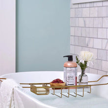 Load image into Gallery viewer, Charcoal Rose body wash placed on a gold bathtub caddy beside a white flower in a small glass vase and a wooden bowl of dried red petals, staged over a white freestanding tub with a blue and white marble wall in the background. 