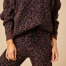 Load image into Gallery viewer, Close-up of a person wearing a soft  espresso-colored lounge set with a black leopard print pattern The pants have a black drawstring. Against a soft beige background. 
