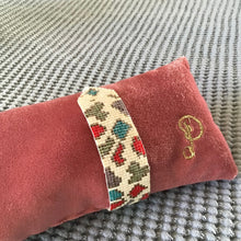 Load image into Gallery viewer, Decorative beaded bracelet band with beaded leopard spots in blue, red, green, and brown, on a pink cushion with a &quot;P&quot; embroidery. Ona gray textured surface.