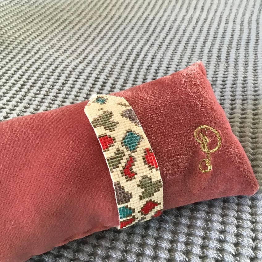 Decorative beaded bracelet band with beaded leopard spots in blue, red, green, and brown, on a pink cushion with a 