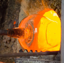Load image into Gallery viewer, Molten glass glowing orange on a blowpipe inside a furnace during hand-blown glassmaking. 