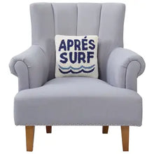 Load image into Gallery viewer, Square off-white hooked wool throw pillow with "APRES SURF" in navy lettering and a wave design displayed on a light upholstered armchair, against a white background.  