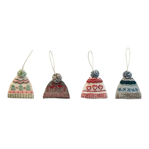 Set of four wool beanie ornaments with pom-poms, each featuring a different knit pattern and color combination. Designs include green and pink scallops, brown with red reindeers, cream with red hearts, and blue with snowflakes. Each ornament has a hanging loop and is displayed against a white background.  