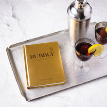 Load image into Gallery viewer, Gold cocktail recipe book "BUBBLY" by Colleen Jeffers shown with a silver shaker and dark red cocktails in stemmed glasses. 
