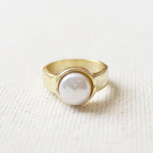 Load image into Gallery viewer, 14K gold semi-matte double plated brass casting ring with a white freshwater pearl in a bezel setting. Ring is resting on a cream woven fabric surface.