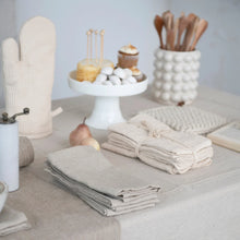 Load image into Gallery viewer, A set of beige linen and cotton cocktail napkins displayed on a table with other kitchen items in the background.