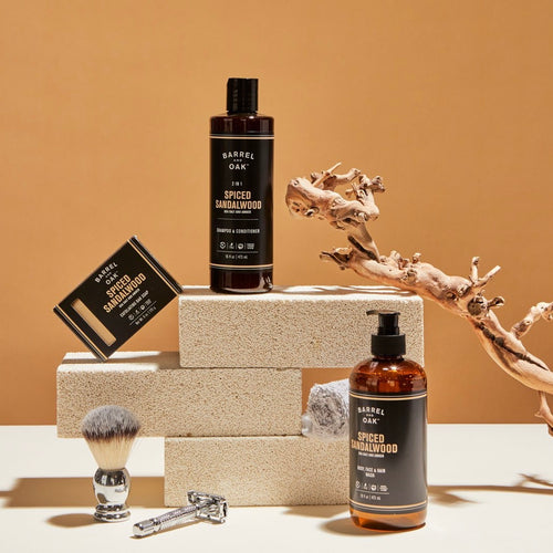 Mens soup products in amber bottles placed on cement bricks. Arranged with a tree branch and shaving items all on a white platform with an brown wall as the background. 