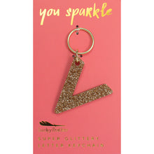 Load image into Gallery viewer, Gold glittery letter &quot;V&quot; keychain on a pink card with &quot;you sparkle&quot; in gold text, displayed against a white background.
