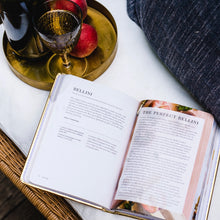 Load image into Gallery viewer, Open "BUBBLY" cocktail book displaying Bellini recipe with brass tray, textured goblet, and fresh peaches nearby. 