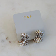 Load image into Gallery viewer, Gold-plated huggie earrings adorned with clustered pearl beads and clear crystal accents, displayed on a light gray jewelry card with "TAI" in gold print on a white background. 