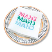 Load image into Gallery viewer, Stack of white cocktail napkins printed with the word "MAHJ" in pink, green, and blue, displayed on a decorative round plate with a gold and dark gray patterned border.