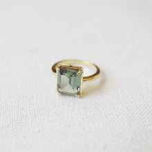 Load image into Gallery viewer, Gold-plated brass ring featuring a rectangular emerald-cut green tourmaline spinel stone set in four prongs, displayed on a soft white textured surface. 