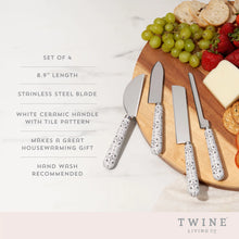 Load image into Gallery viewer, Black-and-white tile-patterned stainless steel cheese knife set of four with stainless steel blades and ceramic handles, shown on a wooden board with assorted cheeses, crackers, and fruit  alongside specifications including 8.9-inch length and hand-wash care details. 