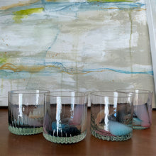 Load image into Gallery viewer, Speak EZ Cups hand-blown glass set of four with heavy textured bases and assorted peach, steel blue, pink, and mint accents on wooden surface against abstract background. 